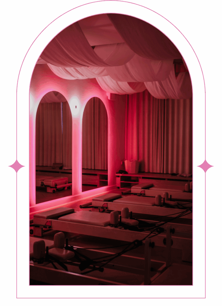 Przepiękne wnętrze butikowego Studio Pilateska w Suwałkach z nowoczesnymi drewnianymi maszynami do pilatesu (reformer). Klimatyczne, przytłumione oświetlenie sprzyjające relaksowi z nadaną maską łuku